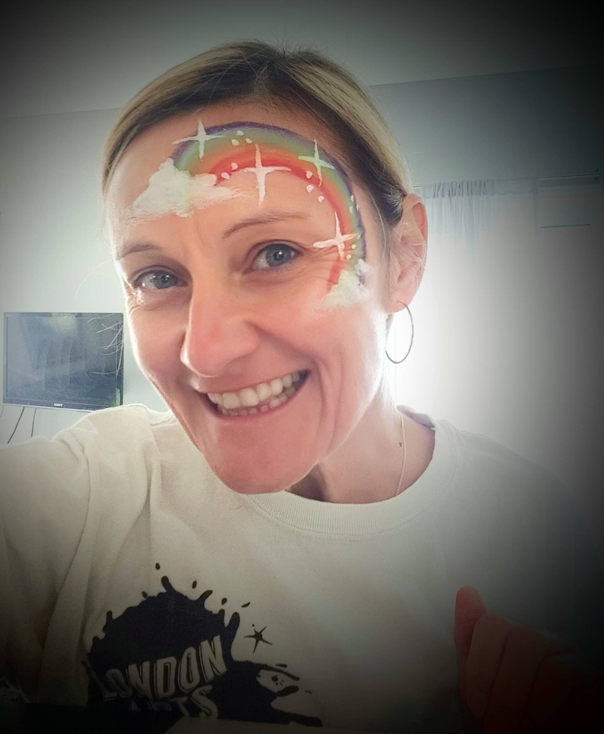 Bronagh Joyce Morgan grinning with a rainbow painted across her forehead at a community arts event.